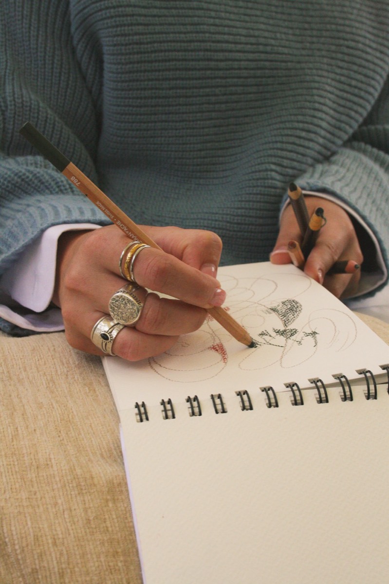 Hands sketching a flower in a spiral notebook